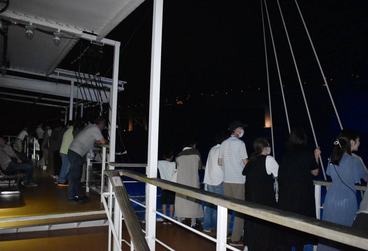 甲板から夜の海を眺める乗船客たち